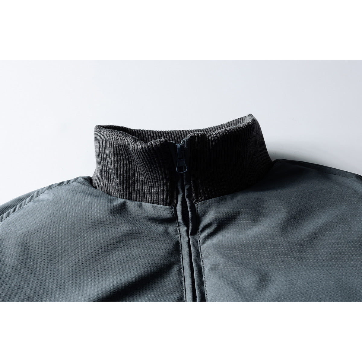 Close-up of a charcoal gray jacket's ribbed high collar and front zipper.