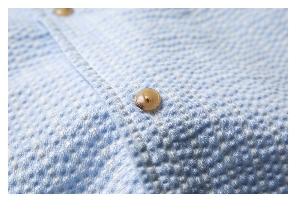 Close-up of a tan button and stitched placket on the pale blue textured shirt.