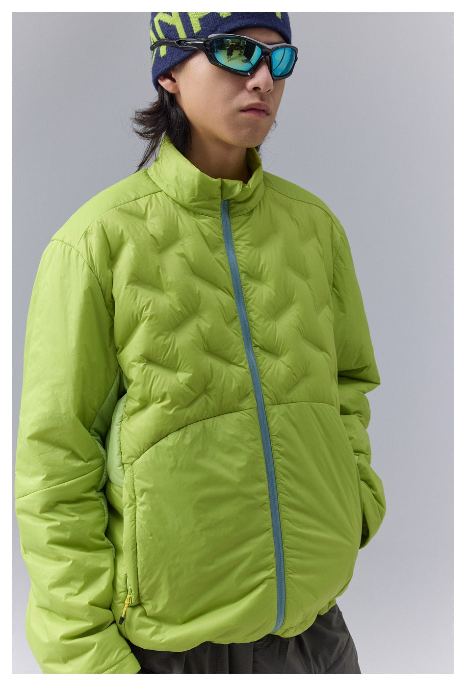 Close-up of a model wearing a lime green jacket, showing the wavy quilting, gray-blue zipper and stand collar