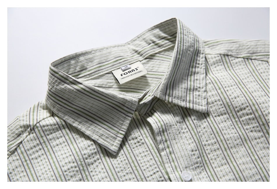 Close-up of the pointed collar and upper front of an off-white shirt with fine gray and muted green stripes.
