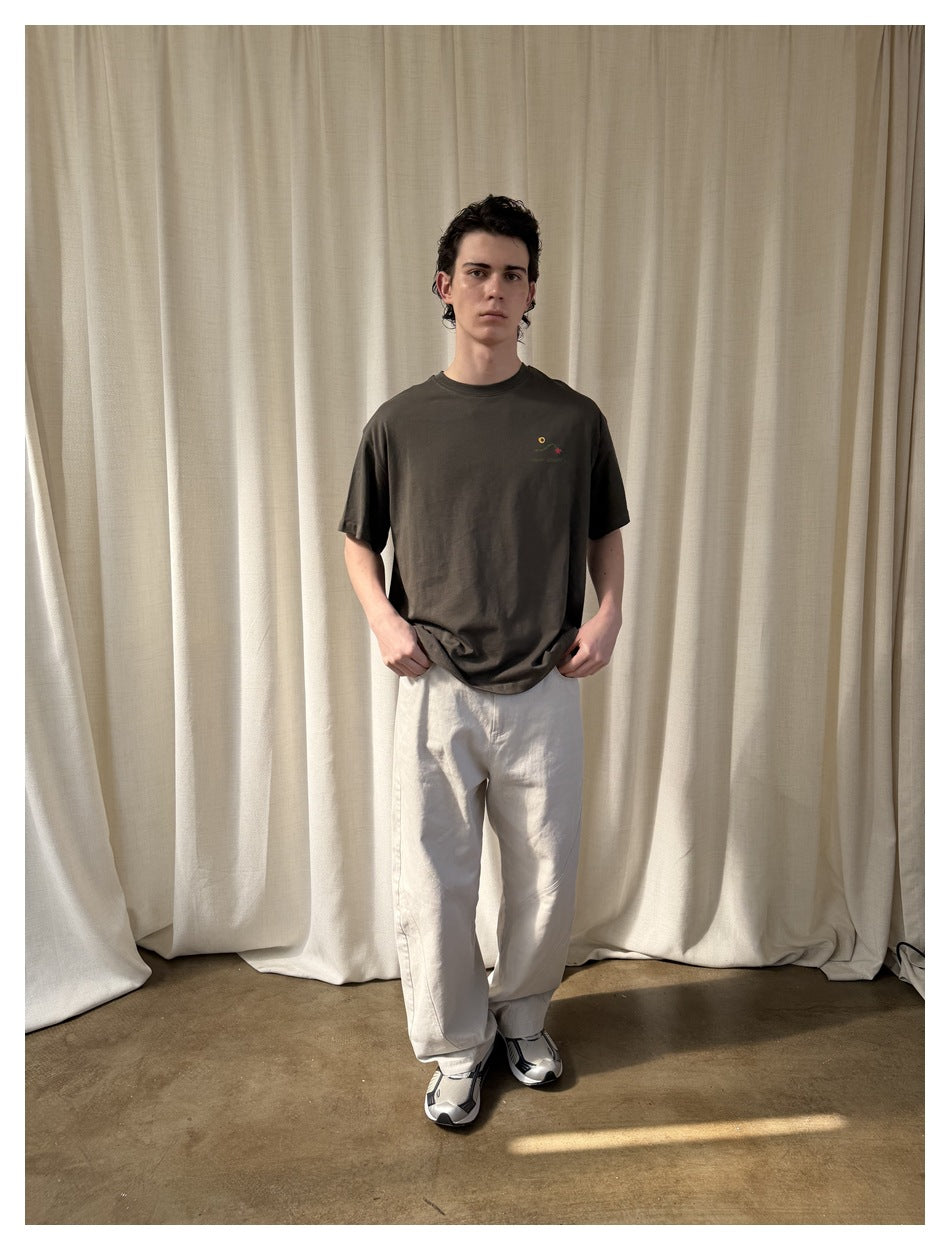 Model wearing a charcoal brown oversized T-shirt with a small multicolor chest graphic, shown from the front.
