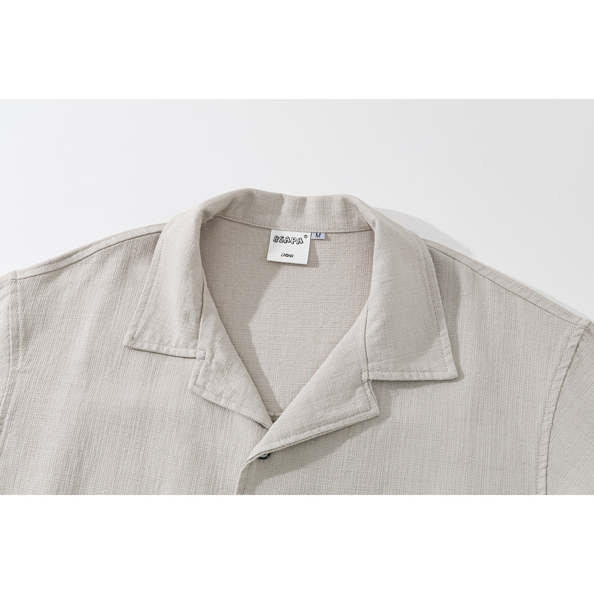 Close-up of a light beige short-sleeve shirt's notched collar and neckline, with the sewn-in neck label visible.