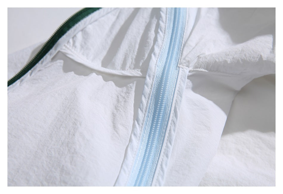Close-up of a pale blue zipper on white crinkled fabric beside dark green trim.