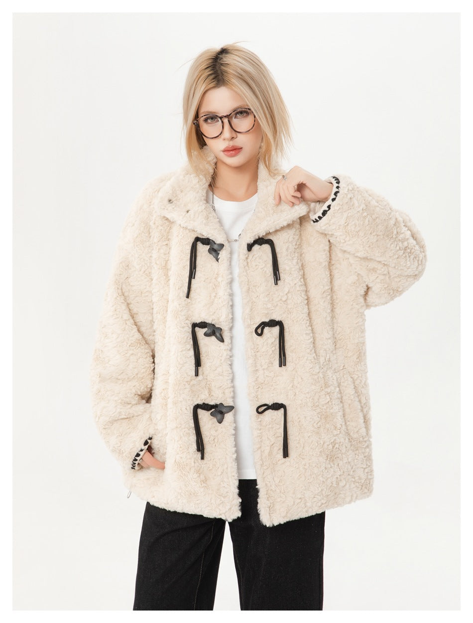 Close-up of model in cream textured jacket with black butterfly toggles and contrast cuff trim