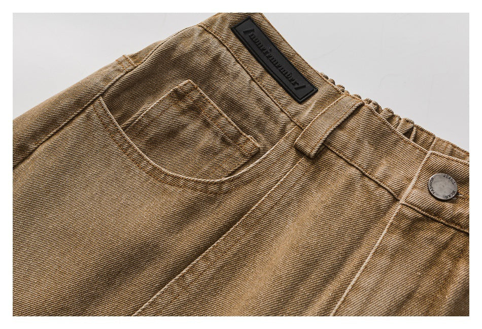 Close-up of the waistband, front pocket, button, and stitched details on tan washed jeans.