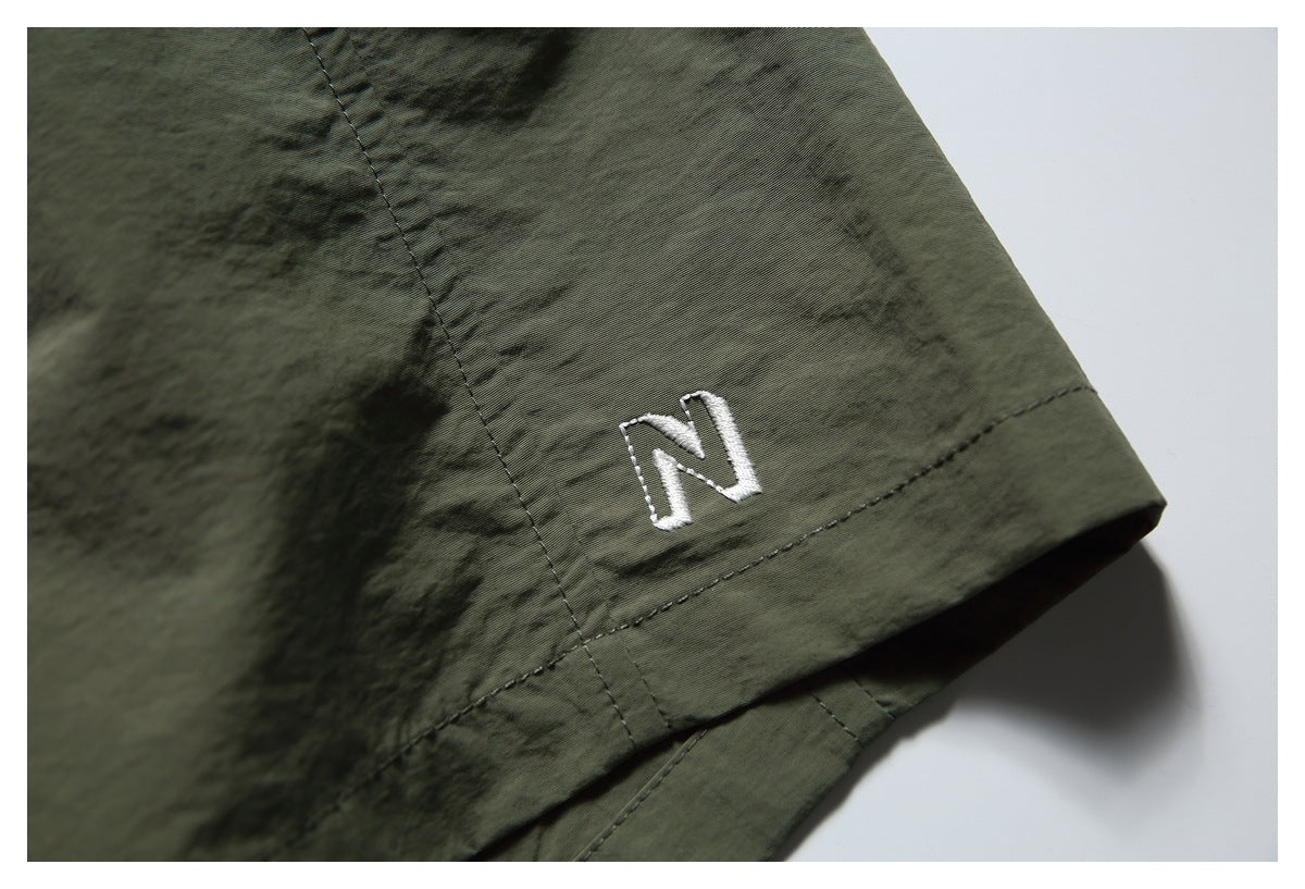 Detailed view of a white embroidered N near the hem of olive shorts.