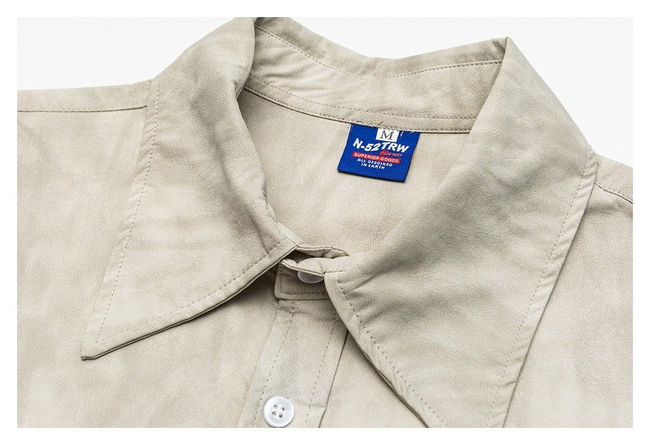 Close-up of the beige shirt's pointed collar, top button, and woven neck label.