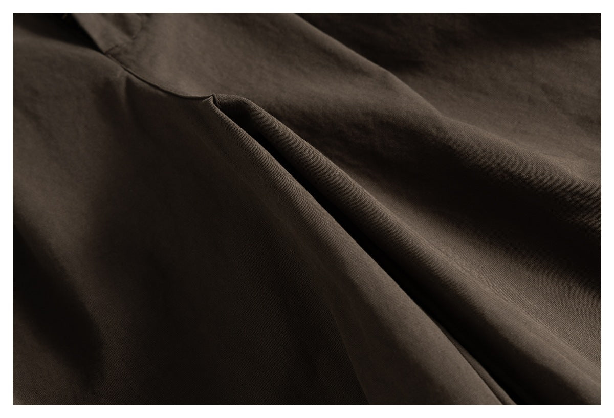 Close-up of brown trousers showing a slanted pocket opening and surrounding fabric folds.