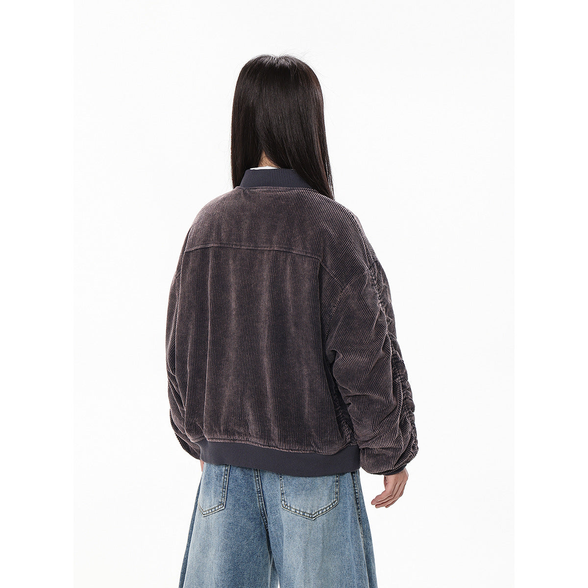 Rear view of a model wearing a dark brown ribbed bomber jacket and loose blue jeans.