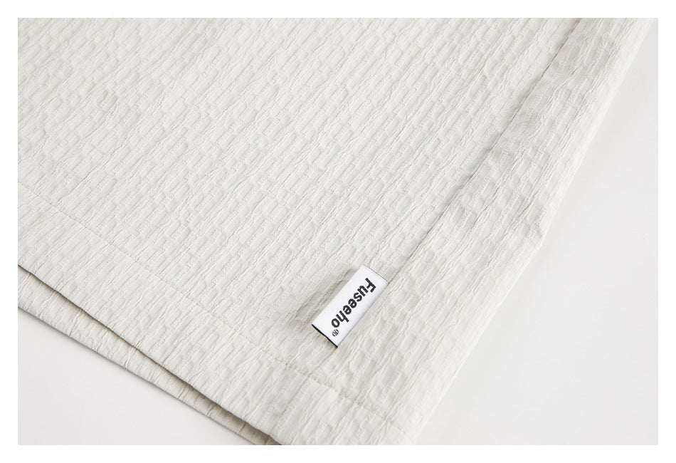 Close-up of the hem and textured off-white fabric of the shorts, with a small sewn label.