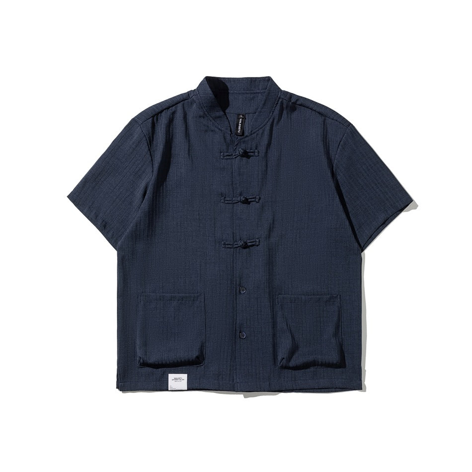 Navy short-sleeve shirt with stand collar, knotted frog closures, buttons and two large front patch pockets, flat lay