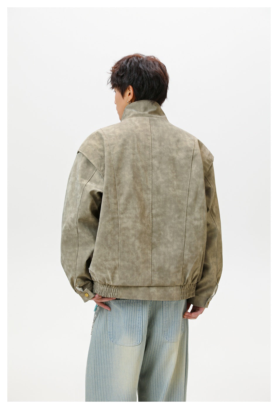 Back view of a model wearing a taupe mottled jacket with a stand collar, seam panels, and an elasticized hem.