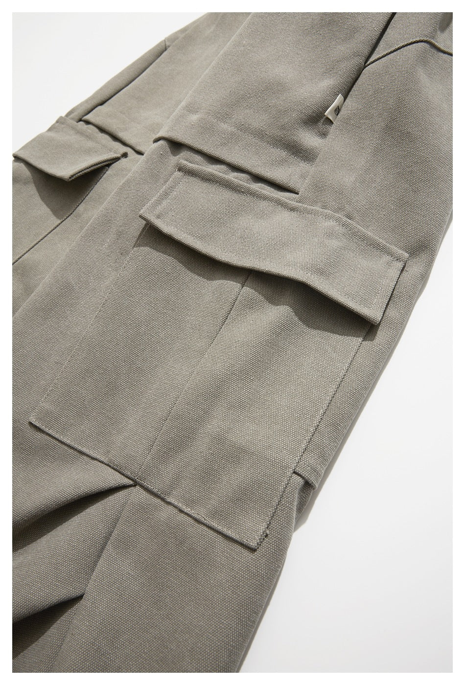 Close-up of taupe-gray trousers with a large flap cargo pocket and a small fabric tag.