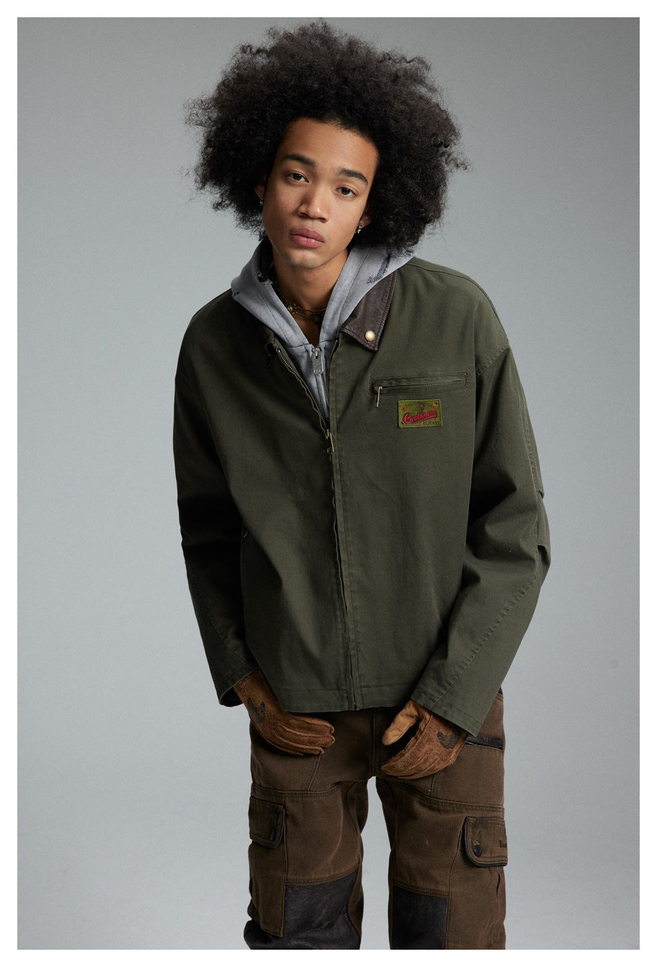 Front view of a model wearing an olive jacket with a brown collar and chest zip pocket over a gray hoodie.
