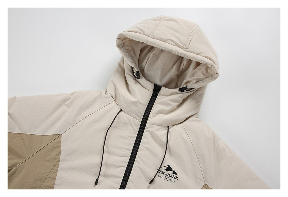 Close view of a light beige hooded jacket with black zipper and drawcords, darker color-block panels, and a chest graphic.