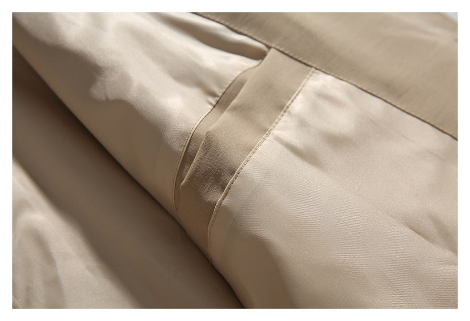 Close-up of a beige coat sleeve with a stitched cuff tab and seam.