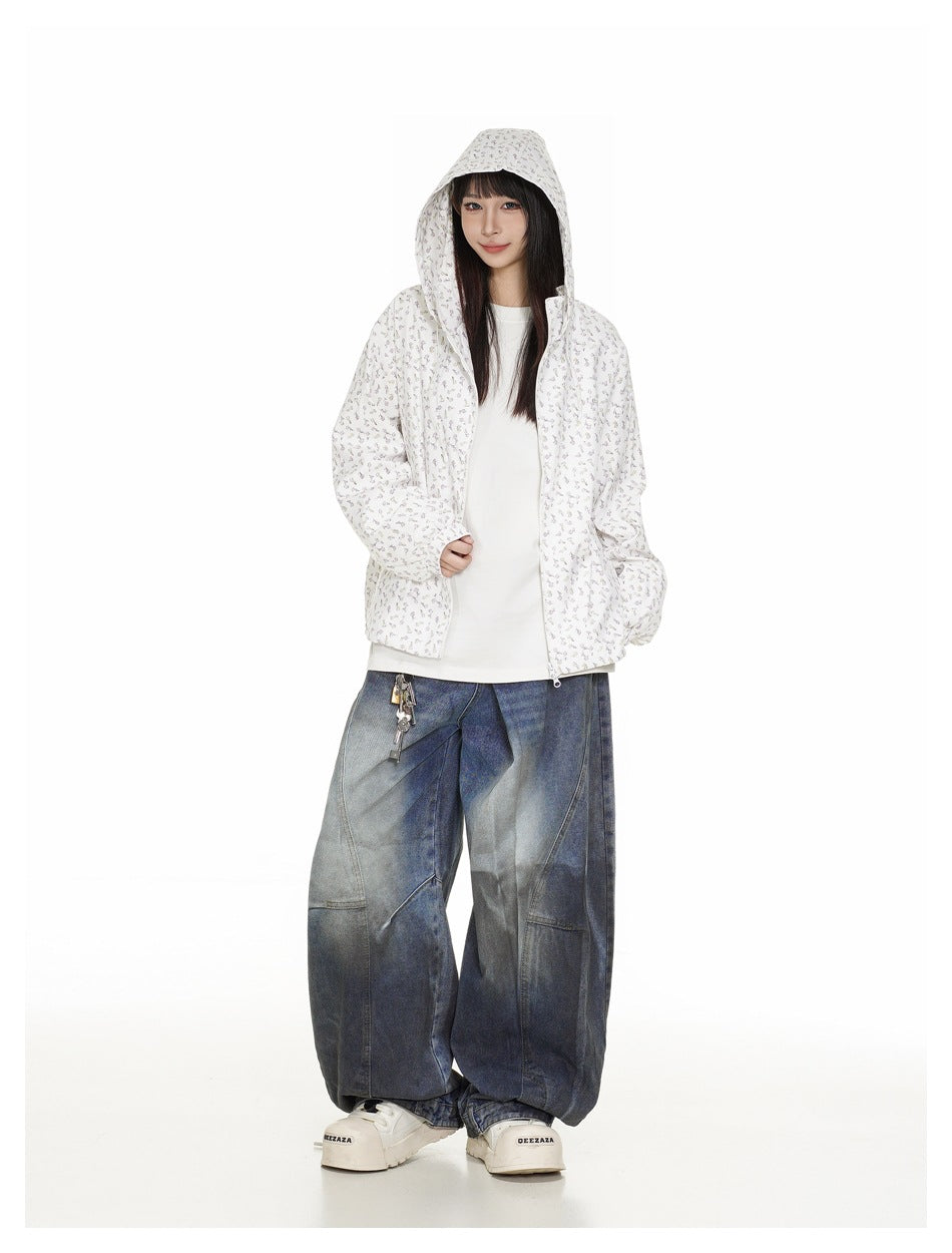 Full-length model wearing a white floral-print zip-up jacket with the hood up and oversized dark blue jeans.