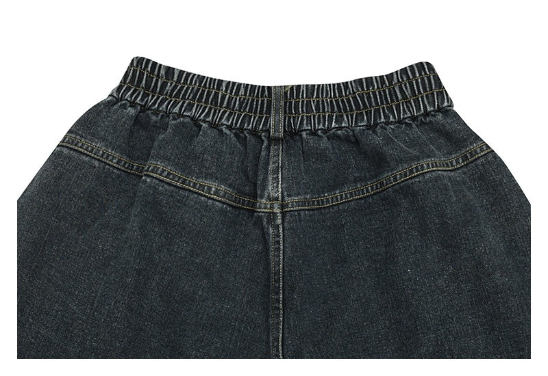 Close-up of dark charcoal denim pants showing an elastic waistband, center seam, and curved yoke stitching.