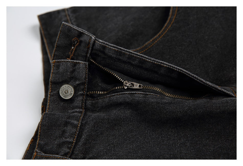 Close-up of dark charcoal jeans at the waist, showing the open zipper, metal button and contrasting stitching.