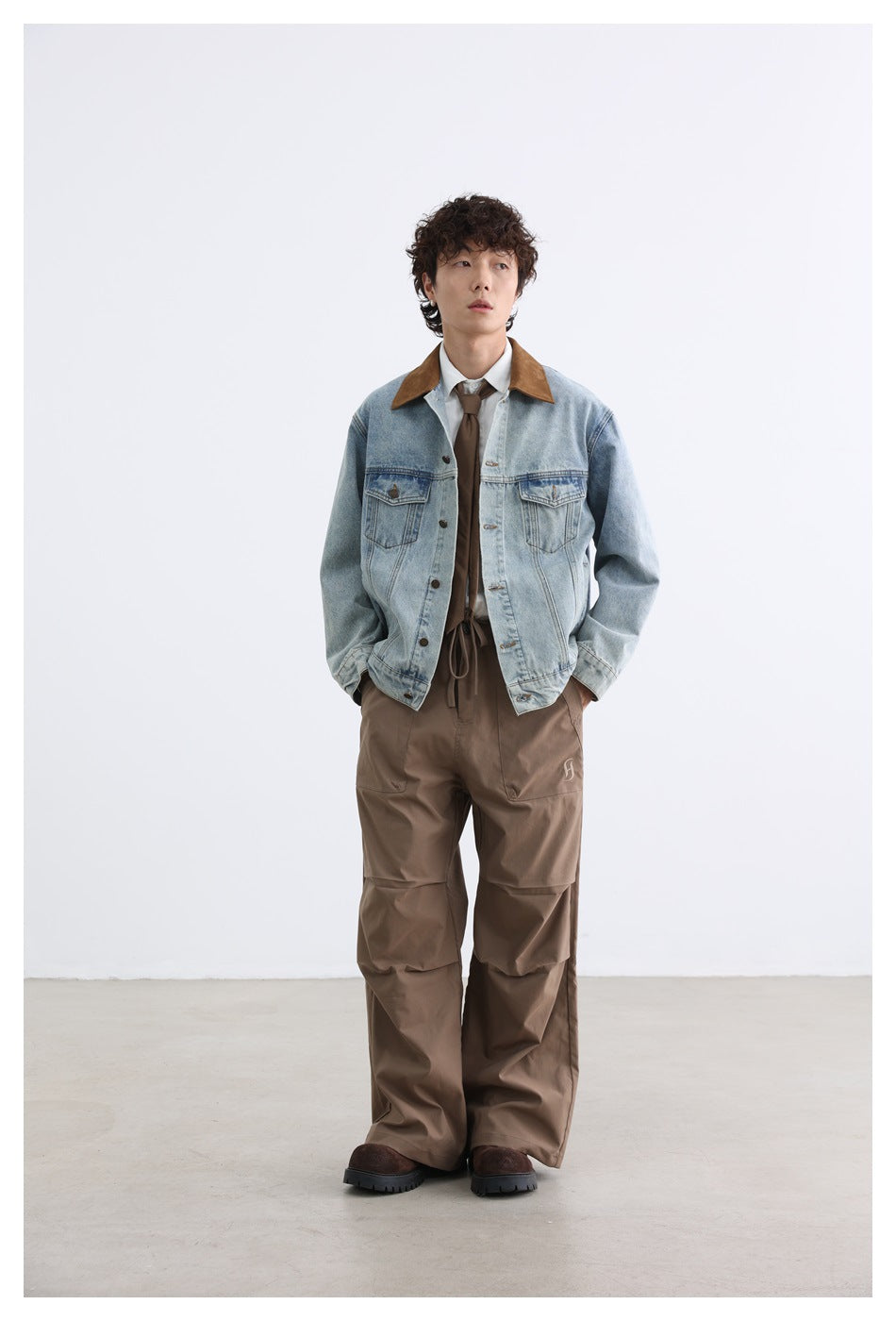 Full-length front view of a model wearing a light-wash denim jacket with a brown collar and loose brown trousers.