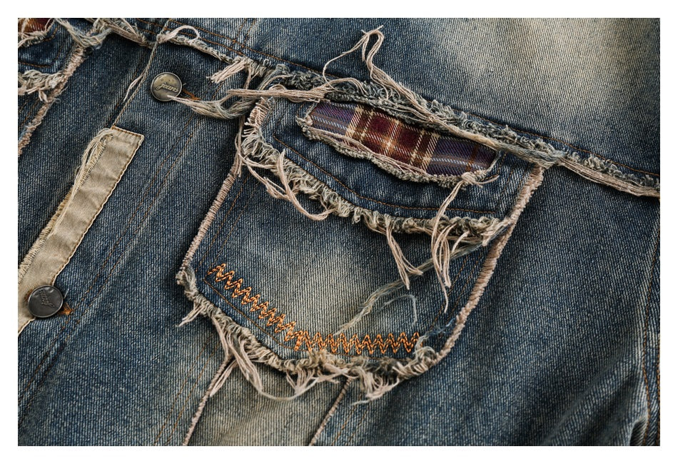 Close-up of a distressed denim back pocket with a plaid insert and orange zigzag stitching.