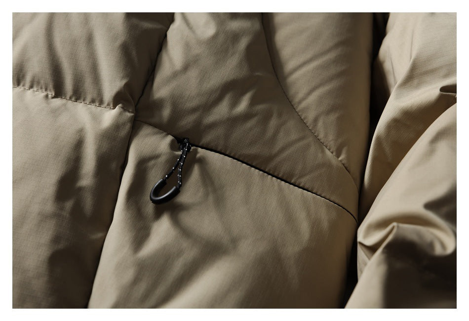 Close-up of a taupe jacket pocket with a black zipper pull and stitched panels.