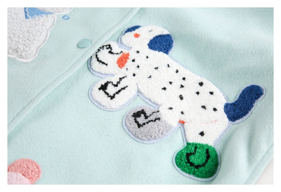 Close-up of a raised white dog appliqué with blue, black, orange and green details on a pale mint coat.