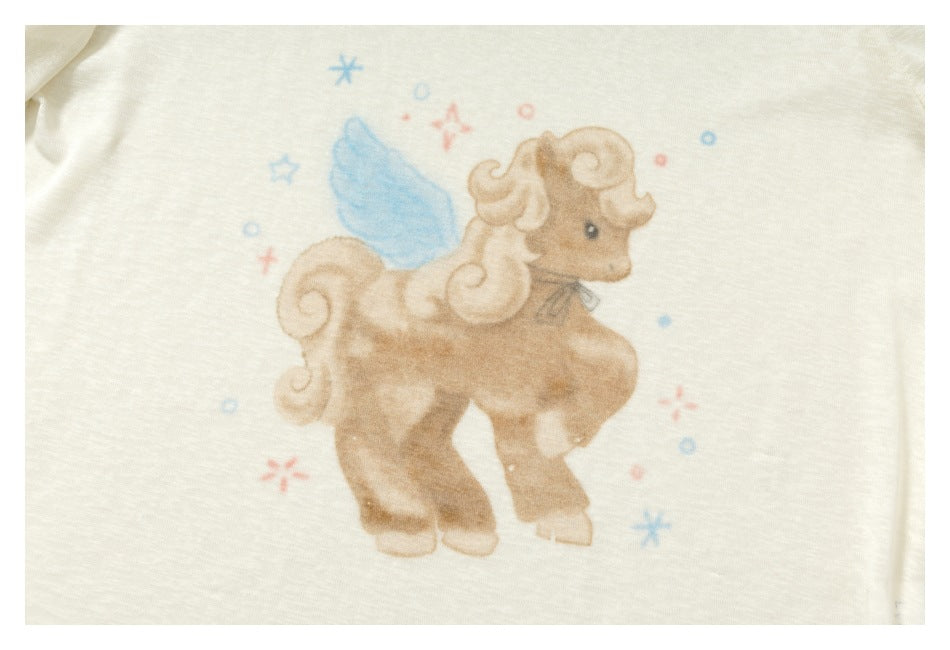 Close-up of a brown winged pony graphic surrounded by small blue and coral motifs on an ivory shirt.