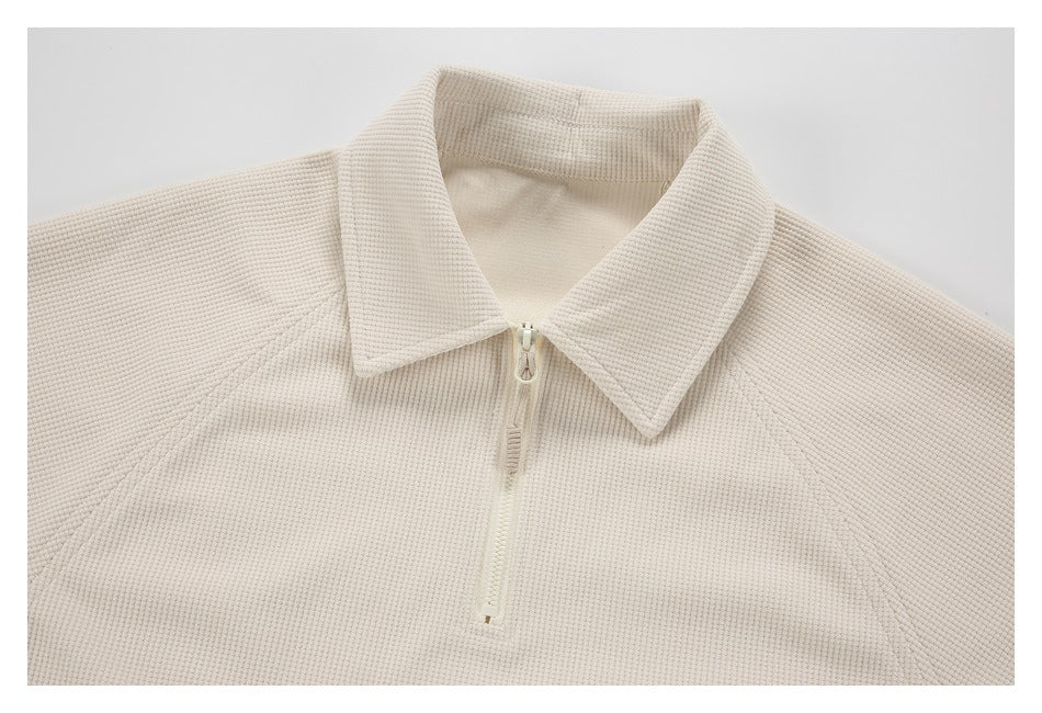 Close-up of a cream quarter-zip top with a pointed collar and textured fabric.