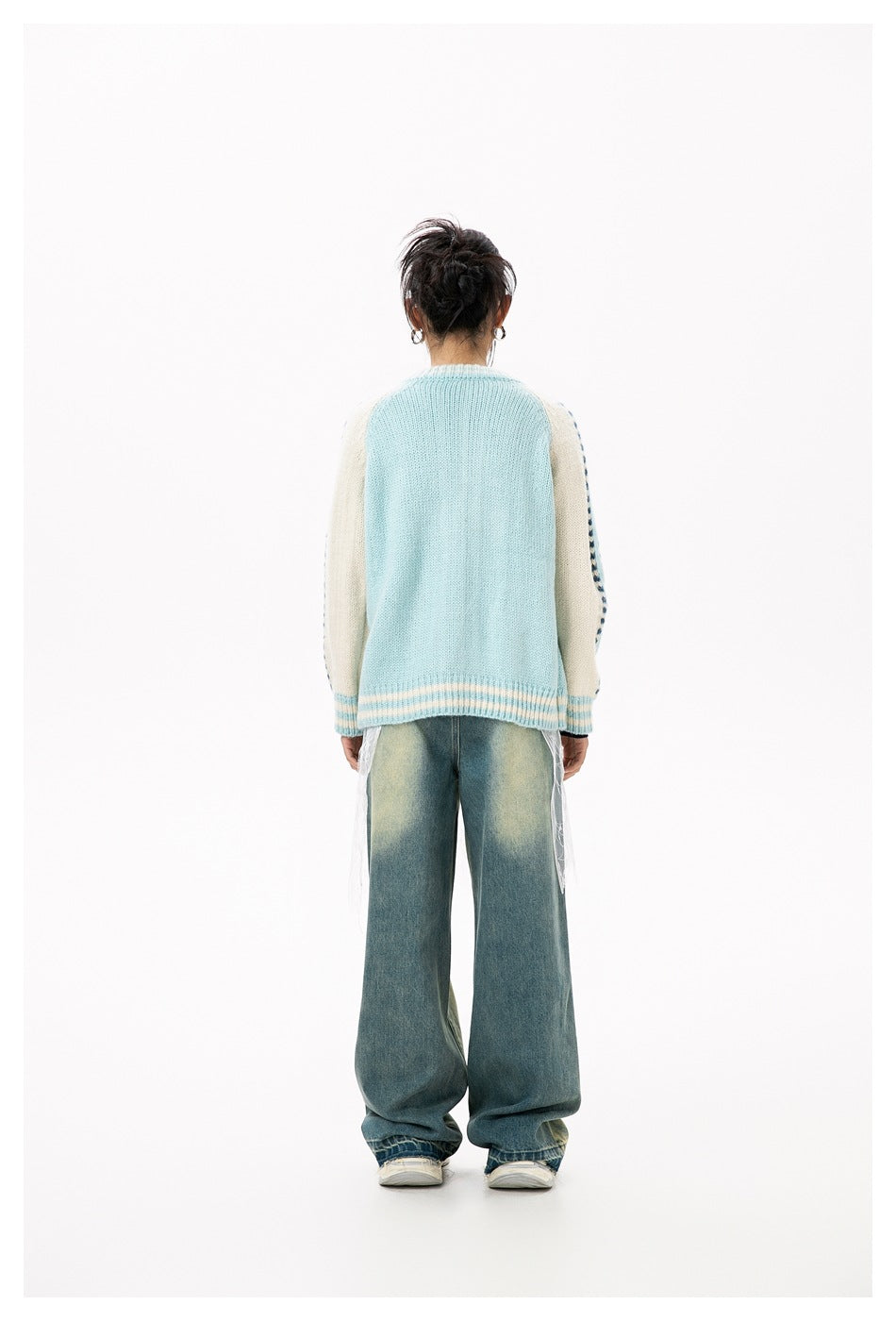 Back view of model wearing the light blue knit cardigan with cream sleeves and striped hem over faded wide-leg jeans