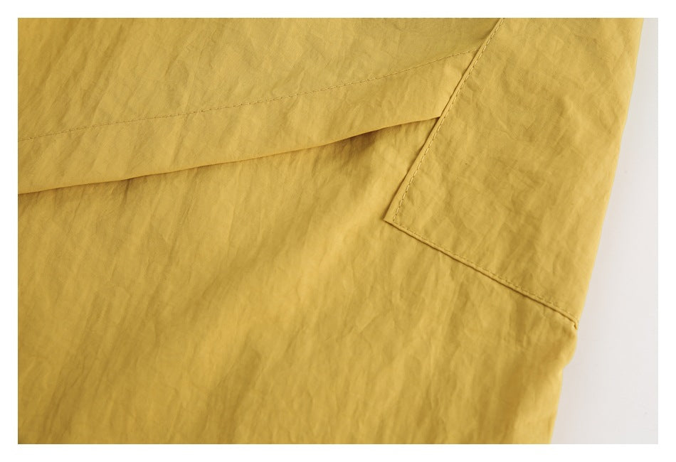 Close-up of mustard-yellow garment showing overlapping stitched panels and a pocket edge.