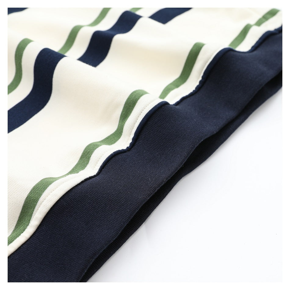 Close-up of cream knit fabric with navy and muted green stripes meeting a wide navy hem.