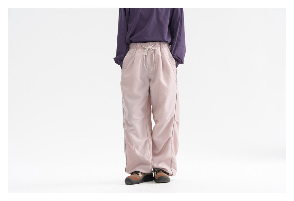 Front view of a model wearing loose pale pink drawstring trousers with side pockets.
