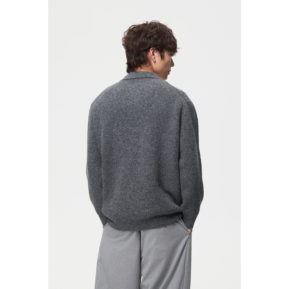 Model shown from behind in a dark charcoal knit polo sweater and light gray trousers.