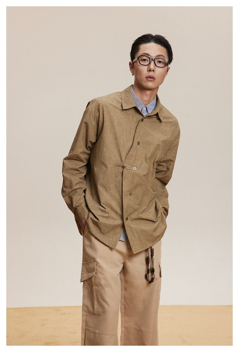 Model wearing a tan button-front shirt jacket with a waist tab over beige cargo pants.