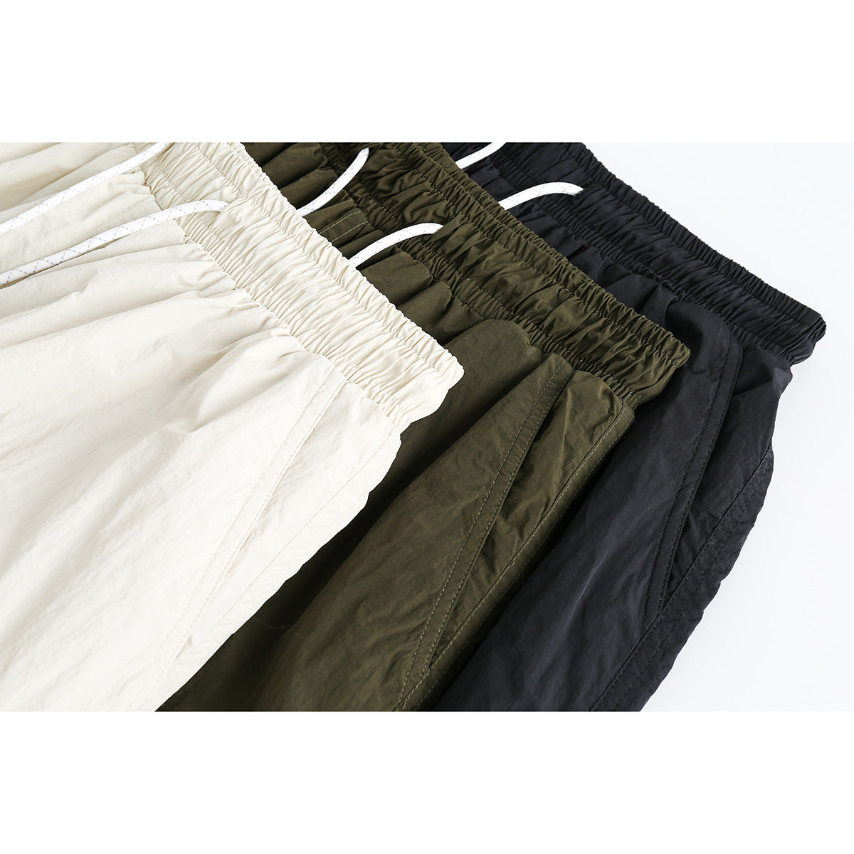 Close-up of cream, olive, and black shorts showing elastic waistbands and white drawstrings.