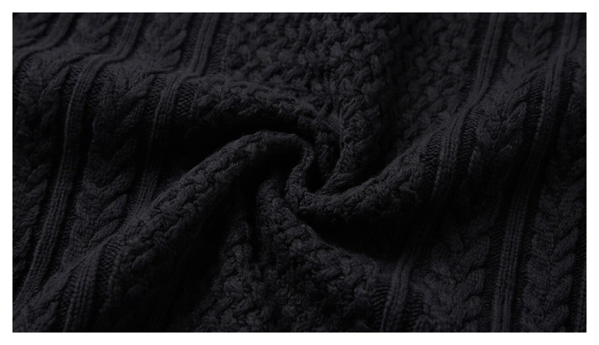 Macro view of black sweater knit, showing raised cable patterns and a folded section.