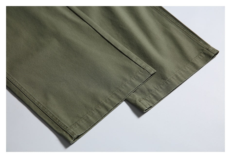 Close-up of the stitched hems of olive trouser legs laid flat.
