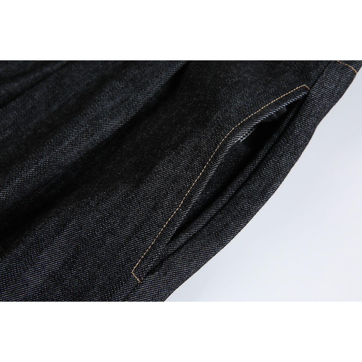 Close-up of a slanted pocket on dark indigo jeans with tan contrast stitching.