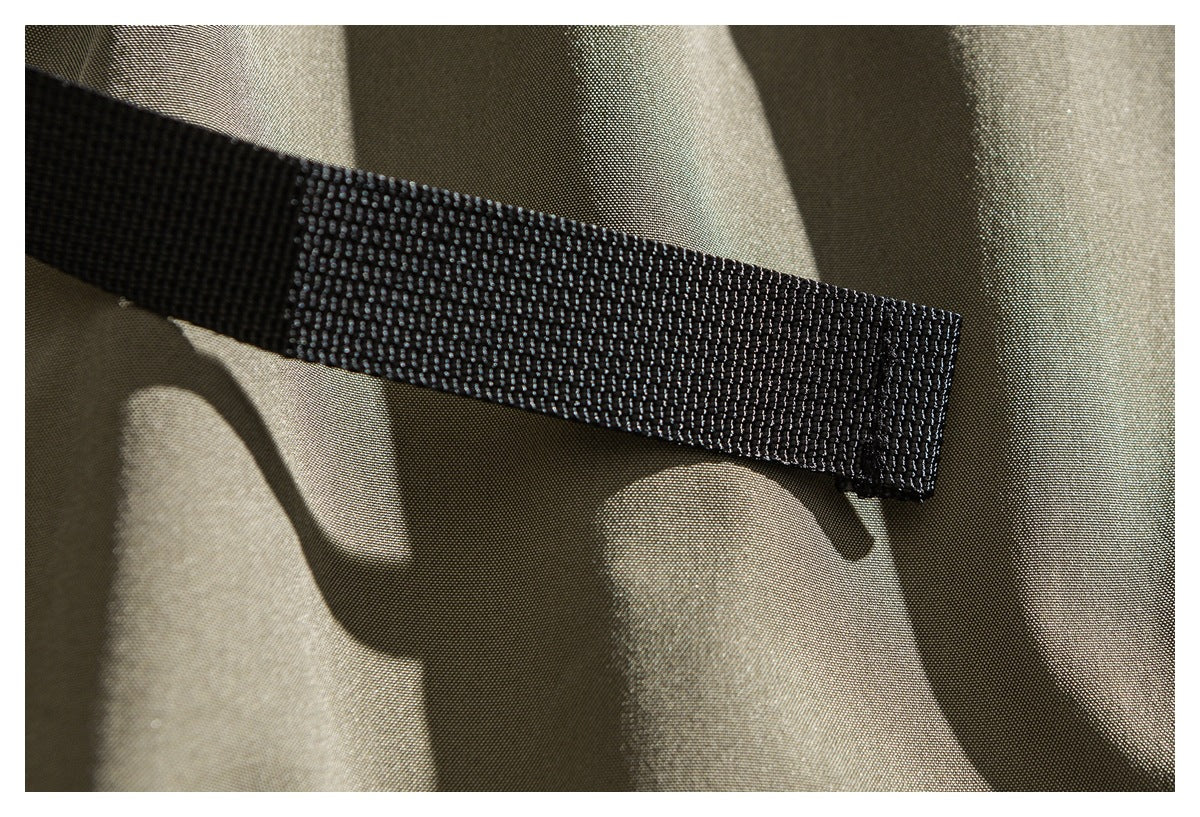 Close-up of a black webbing strap against khaki trouser fabric.