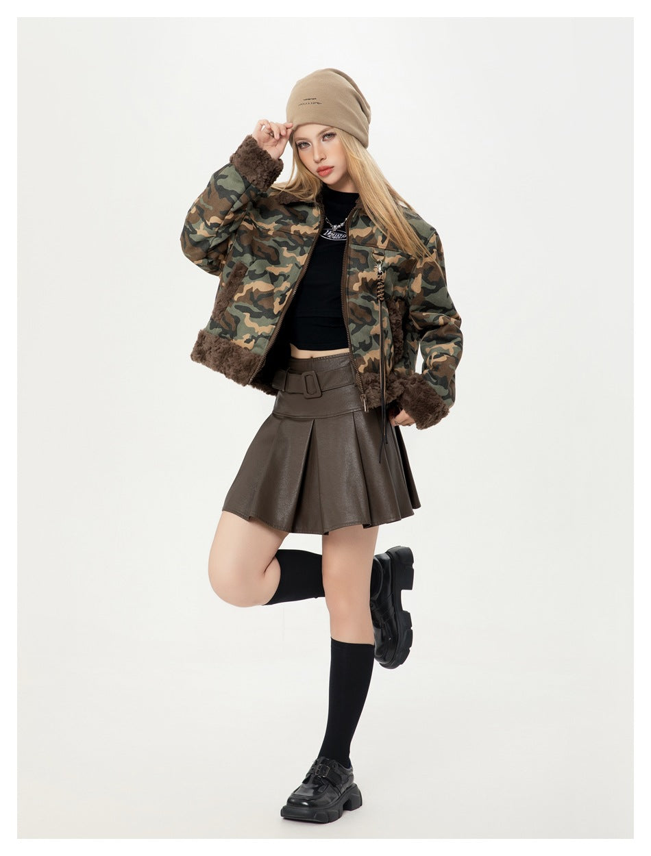 Model wearing an open camouflage jacket with brown fleece-like trim over a black top and brown pleated skirt