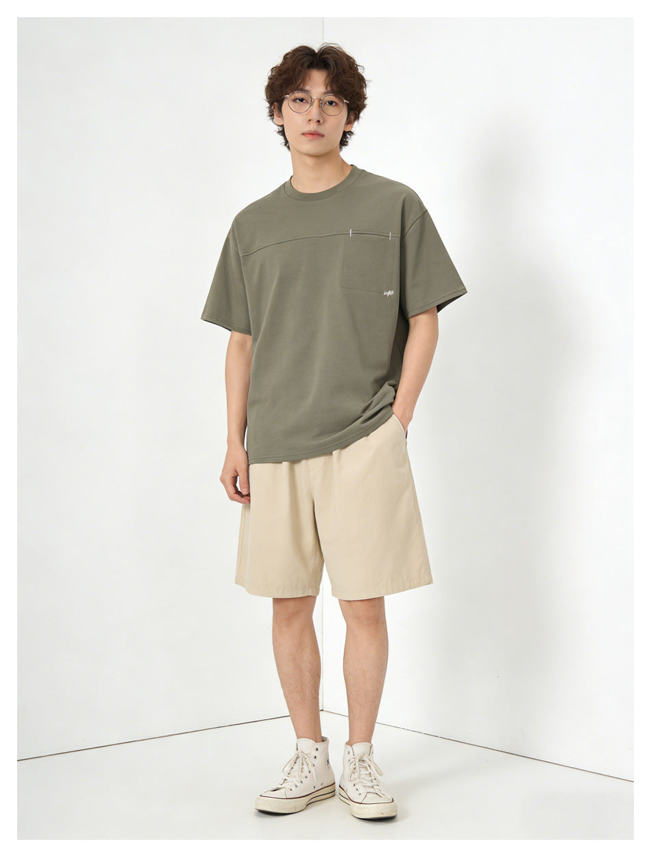 Model wearing an olive green relaxed T-shirt with chest pocket, beige shorts and cream high-top sneakers