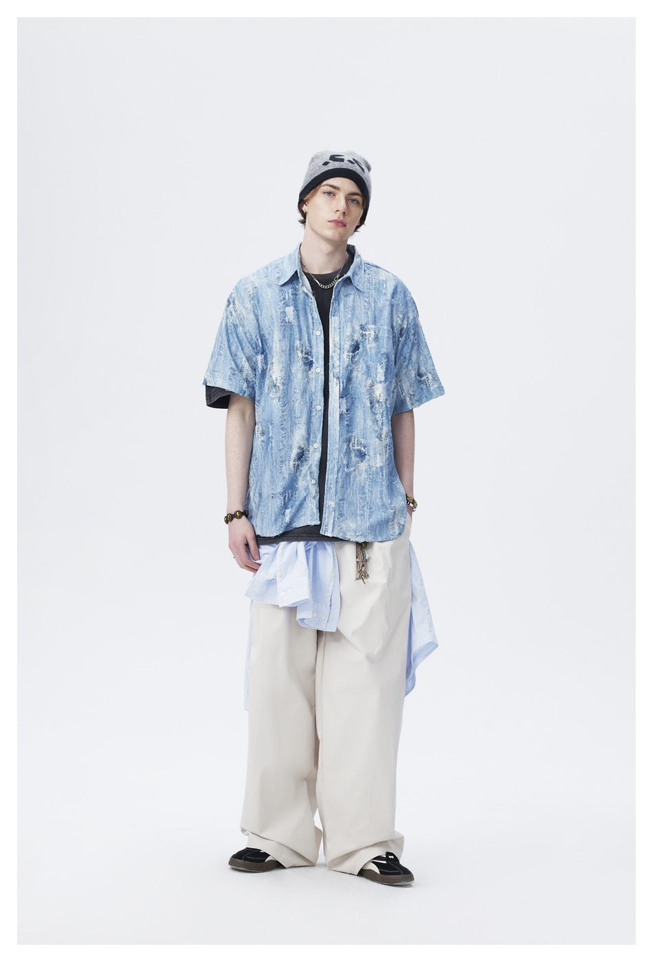 Front view of a model in a blue distressed-pattern short-sleeve button-up, black tee, and loose cream trousers.