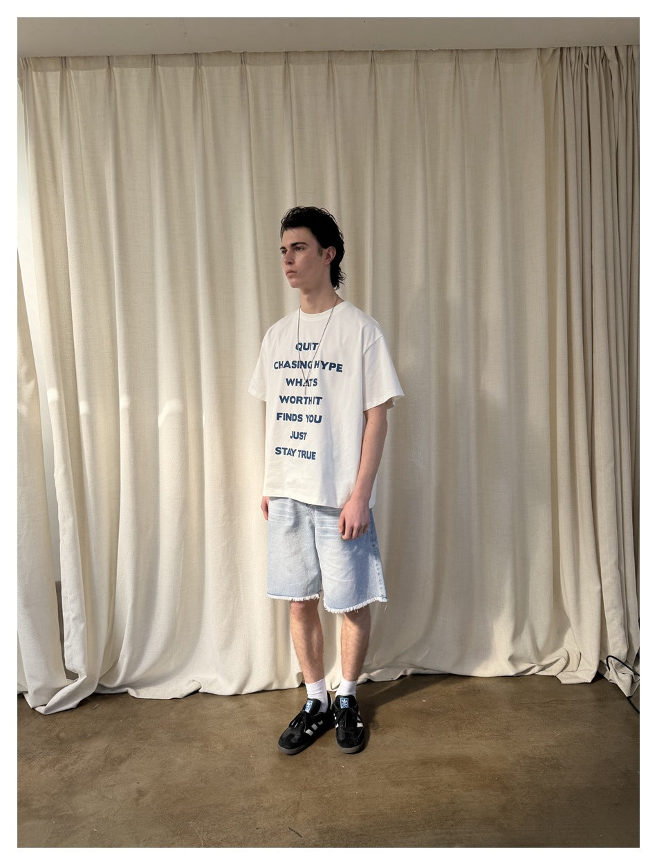 Model in the off-white slogan T-shirt with light denim shorts, three-quarter side view in front of a cream curtain