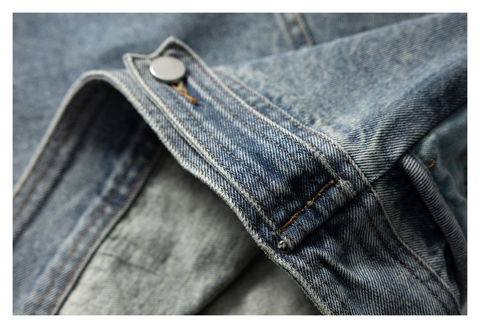 Close-up of a silver button fastening a stitched denim tab beside piped edging.