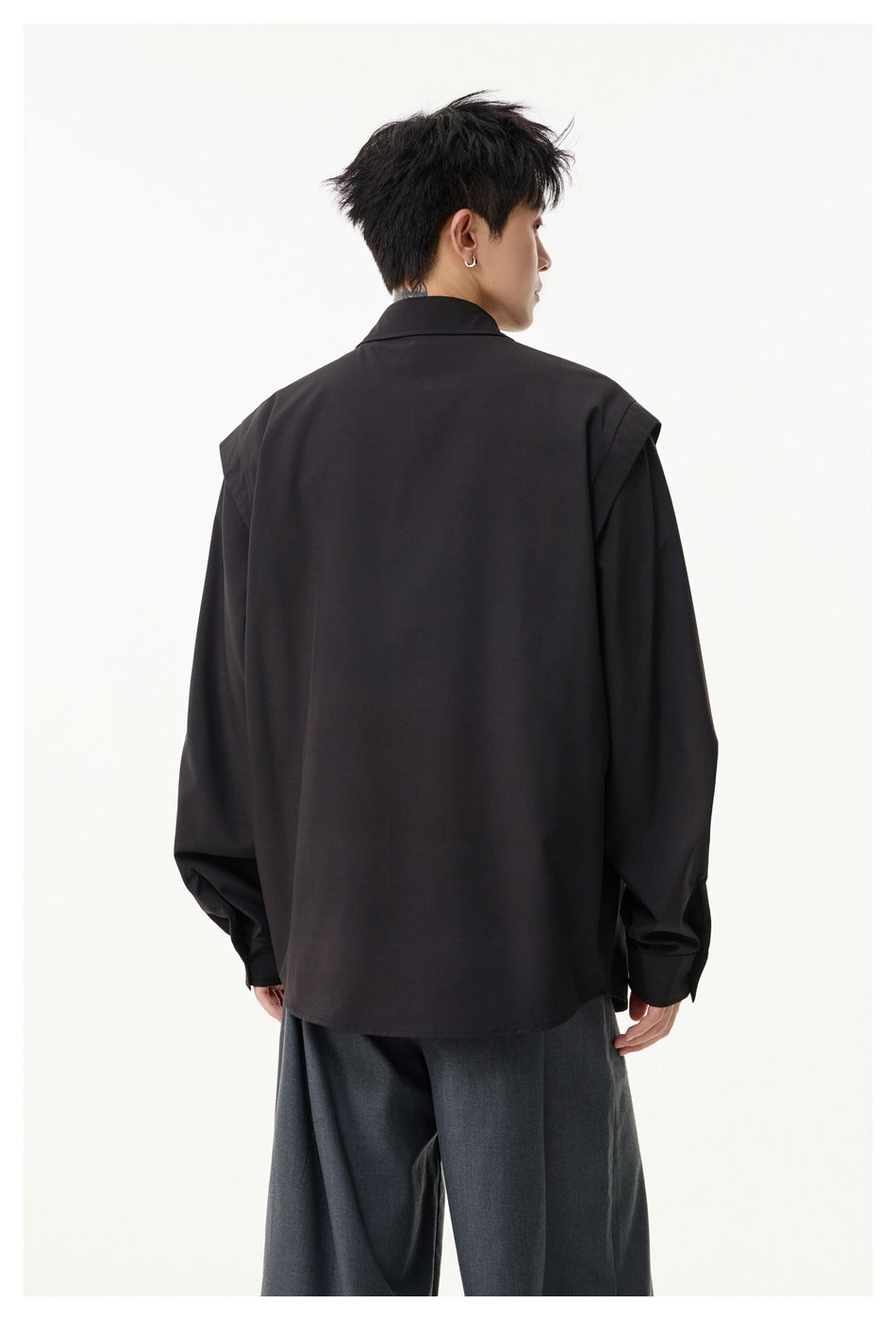 Rear view of a model wearing a black long-sleeve shirt with shoulder details and gray trousers.