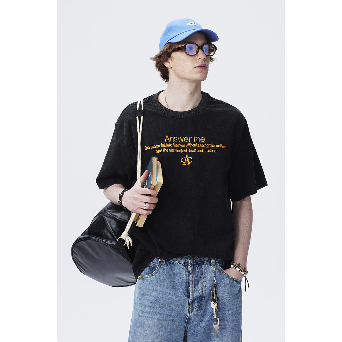 Model wearing a black T-shirt with yellow English text and light blue jeans; shown from the waist up.
