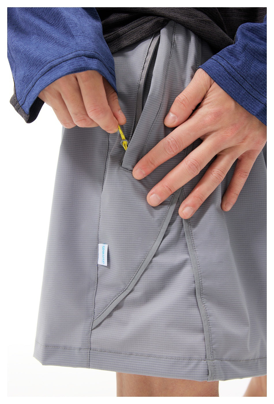 Close-up of a gray shorts pocket with a concealed yellow zipper pull and stitched paneling.