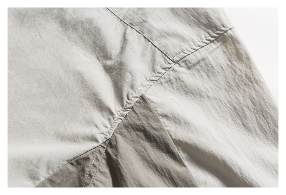 Close-up of light gray-beige garment fabric with intersecting curved stitched seams.