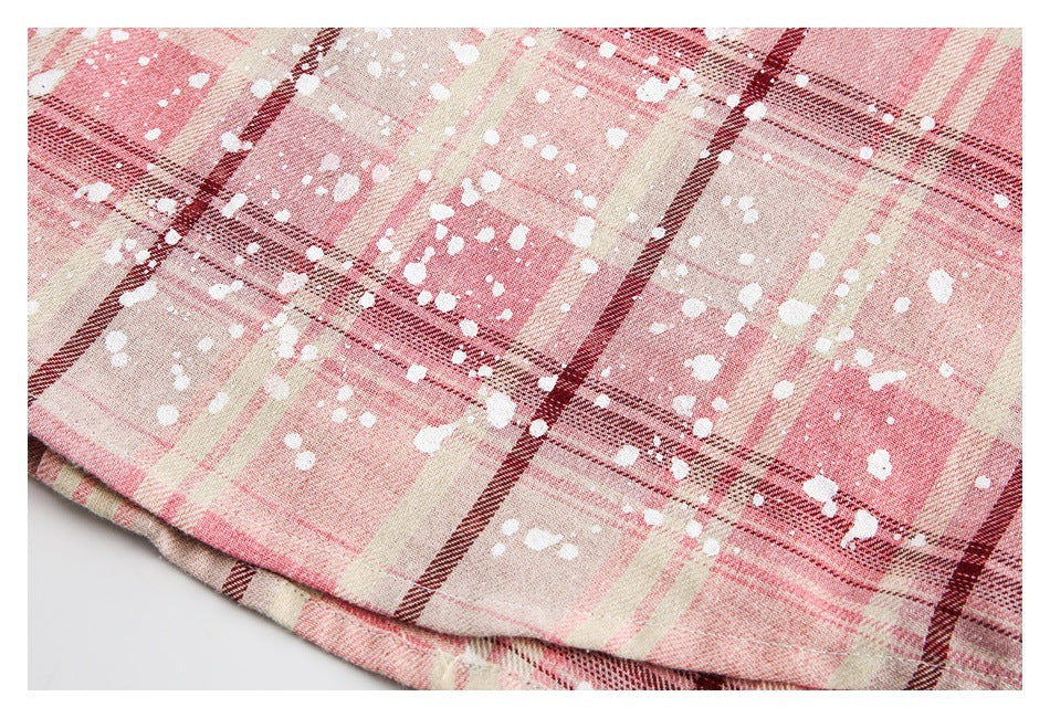 Close-up of pink, cream, and burgundy plaid fabric with scattered white flecks and a folded edge.
